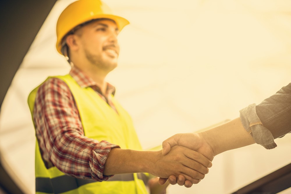 Travailleur de la construction portant un casque et un gilet jaune, serrant la main d'une autre personne
